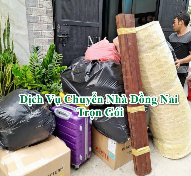 một người đang vận chuyển một valy màu tím, ba túi đồ màu đen, hai thùng cartong, một nệm, một bó thanh gỗ phía trước nhà